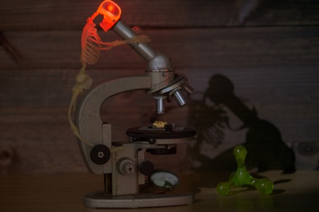 concept photo of scientist in form of skeleton discovering something at the lab looking at microscope. red light shining in his head as a sign of invention thinking process in progress. low key imageの写真素材