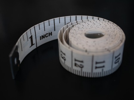 close-up tailor measuring tape isolated on black background. first one inch visible and rest curl up rolled in round coil bobbin spiralの写真素材