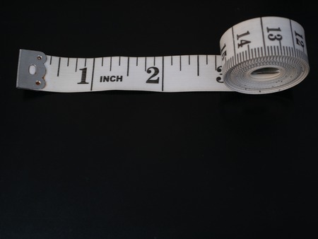 rolled measure tape with inches numbers on dark black background and lot of copy space. can be easily isolated cutoutの写真素材
