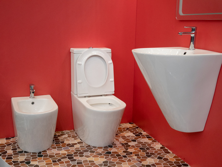 modern home bathroom interior design with white washbasin, toilet, bidet and vivid red wallsの写真素材