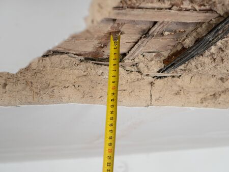 ceiling with peeled plaster stucco and tape measure for measuring volume of damage. selective focus