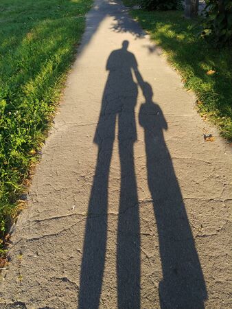 two long shadows of father and son on asphalt sidewalk walking together at summer sunny dayの写真素材