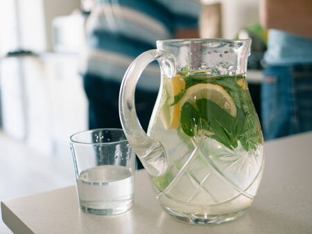 homemade lemonade with lemon wedges slices and mint leaves on a wooden table. blurred people on...