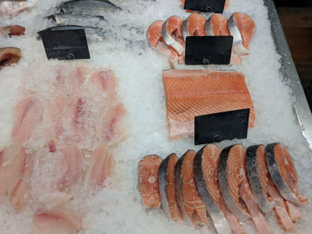 few raw fresh steaks and fillet of red fish on ice with empty price tags at fish market or local...