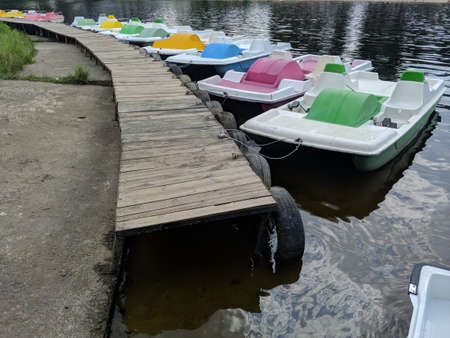 row of a various colorful catamaran boats nearby wooden dock on a lake, river. summer vacation vibes