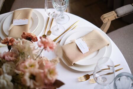Luxury cozy autumn wedding table decoration in the restaurant. Fresh and dried flowers, roses, carnations. Beautiful table setting: golden appliances, fork and knife, calligraphy guest seating card.の写真素材