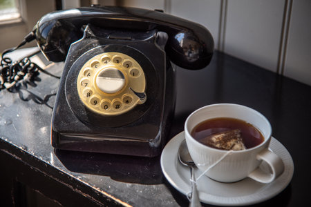 Vintage telephone by the cup of tea on a wooden table.の写真素材