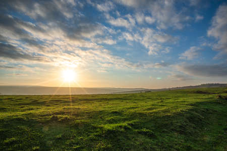 Cold morning sunrise with clouds and blue sky on a green field, East Sussex, UK.