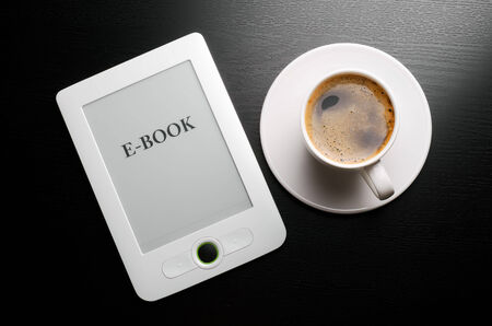 E-book reader and white coffee cup on table