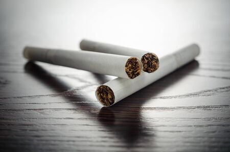 Three white cigarettes on a wooden table closeupの写真素材