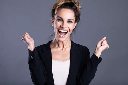 Overjoyed young cute young business woman smiling with joy celebrating win success isolated on gray background. Portrait happy girl.の写真素材
