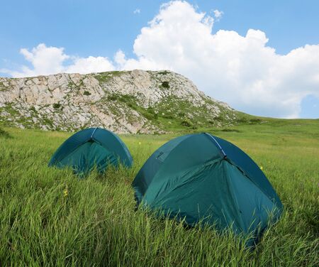 tourists tents on green meadow in mountainsの写真素材