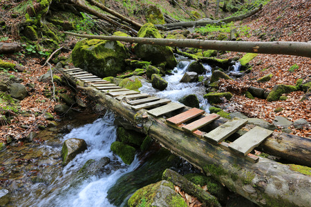 wooden bridge over mountain brook among green stonesの写真素材