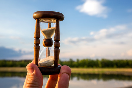 hourglass in hand against sky backgroundの写真素材