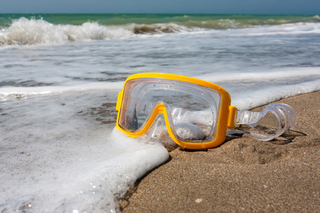 Swimming mask on sea beach in white foamの写真素材