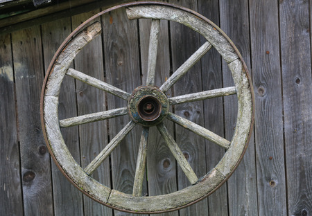 Wheel of an old cart on a wooden wall backgroundの写真素材