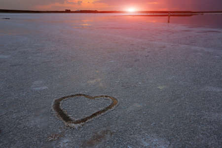 Heart symbol on the surface of a salt lake at sunset background