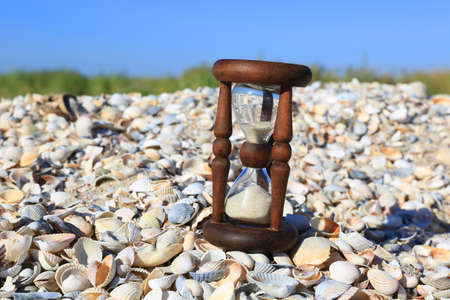ancient hourglass on shells by the sea under blue sky