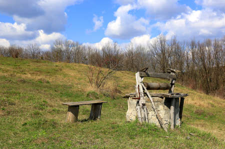 landscape with old well and a wooden bench in a clearing in spring dayの写真素材