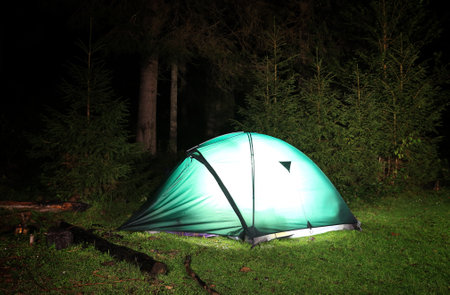 Iluminated tourist tent on meadow in night forestの写真素材