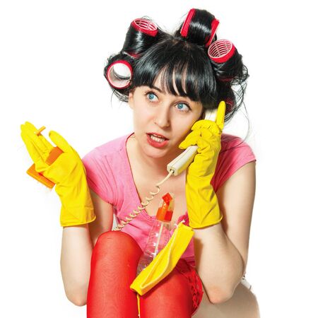 Portrait of a young woman in casual clothing, rubber gloves, hair curlers. She talks on the phone. In her hands the means for cleaning the house and a cigaretteの写真素材