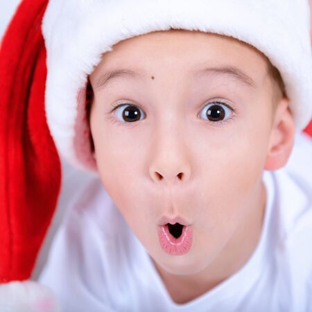 Christmas portrait of a child. Face surprised little boy in a cap of Santa Claus. Photo closeupの写真素材