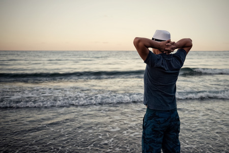 Man looks at the sunset over the sea at the end of a successful day