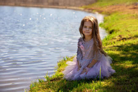 Portrait of a beautiful little girl in summer on nature. Child on the shore of the lakeの写真素材