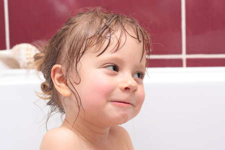 Cute three-year-old girl looking out of a bath and smilingの写真素材