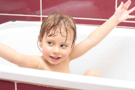 Cute three-year-old girl looking out of a bath and smiling