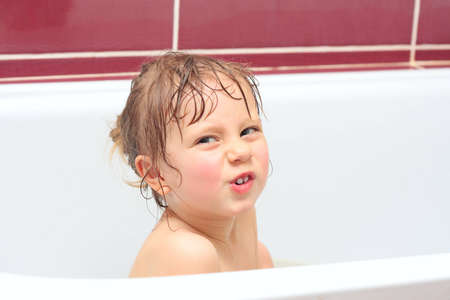 Cute three-year-old girl looking out of a bath and smilingの写真素材