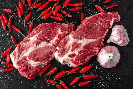 Pieces of raw pork steak with spices and herbs, garlic, salt and pepper on black stone backgroundの写真素材