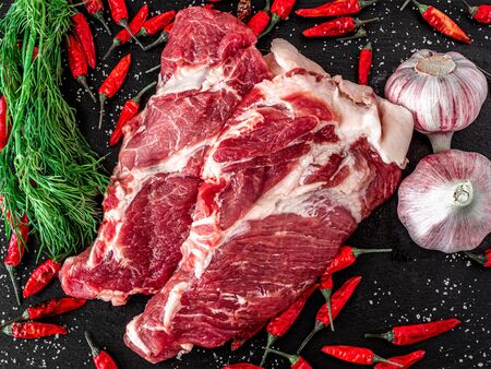 fresh raw meat with spices and rosemary and red pepper on black slate, on dark background, pork, beef, chop on a boneの写真素材