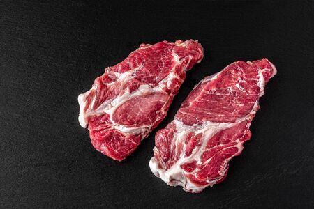 Raw pork meat. Fresh steaks on slate board on black background, neck meat. Top view, horizontalの写真素材