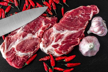 Raw pork meat. Fresh steaks on slate board on black background. meat knife. Top viewの写真素材