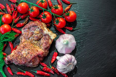 Juicy piece of grilled meat with tomato, garlic and pepper, dark backgroundの写真素材