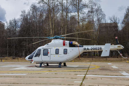 White helicopter sitting on ground, against the background of trees and buildings, horizontalのeditorial素材