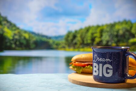 mug of hot coffee on the background of a beautiful mirror lake at sunrise. Morning at the camp. Traveling in a nature park. Tea Cup On Table By Mountain Against Skyの写真素材