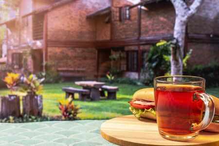 glass cup with tea and a sandwich, in front of a country house, concept breakfast outdoors, buy your house, horizontalの写真素材