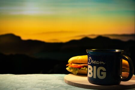 Morning cup of coffee and sandwich with mountain background at sunrise, dream big conceptの写真素材