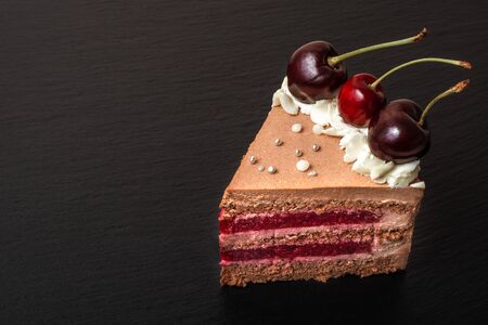 Detail on a Slice Chocolate caramel cake with cherries on black plate. copyspaceの写真素材