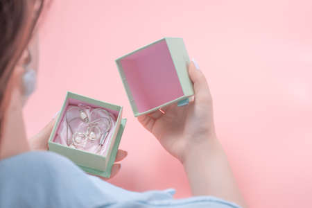 Young woman opens a jewelry gift, in the gift box silver jewelry. present concept, woman holding an open jewelery gift box. pink background. present concept.の写真素材