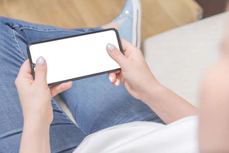 Mockup image of woman's hands holding white mobile phone with blank screen in horizontal position in...