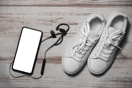 Sneakers and a mobile phone with a blank white screen. cell phone with a blank screen, headphones and white sneakers on wooden background. Mockup.の写真素材