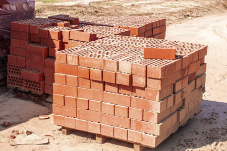 The red bricks are stacked on wooden pallets and prepared for sale. red bricks on a construction site. construction of a building conceptの写真素材