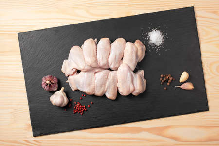 Raw chicken wings. Fresh chicken wings with spices on cutting board. Raw chicken wings with ingredients for cooking on a slate cutting board over wooden background.Top view.の写真素材