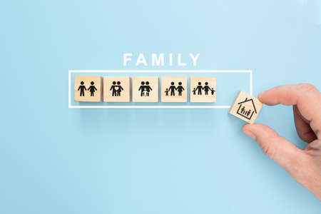 Hand arranging wood cube with family symbol on pastel blue background, copy space. Hand hold wooden block with icon Family Conceptの写真素材
