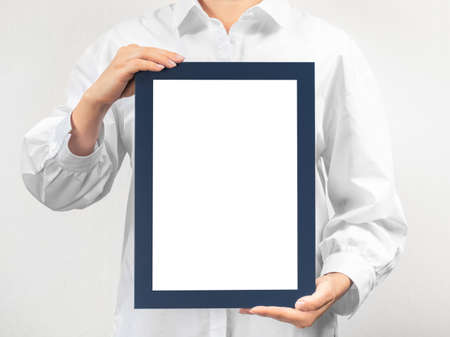 person in white coat holds empty mockup frame. doctor holds and shows the diploma on gray backgroundの写真素材