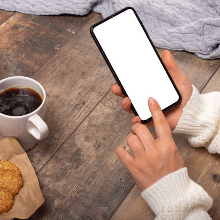 Mockup image of woman's hands holding black mobile cellphone with blank screen on wooden table....