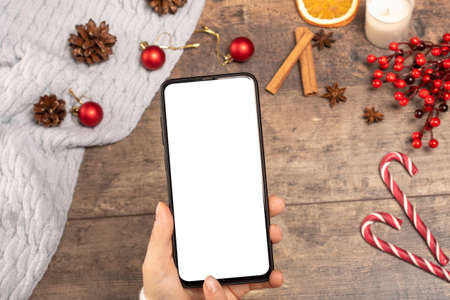mockup cell phone on background wooden table during the Christmas holidays. woman holds a mobile...